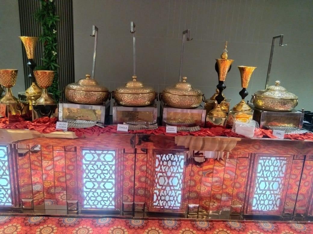 Engraved brass handis labelled Aloo Gobhi, Chole, Shahi Paneer and Dal on a buffet counter