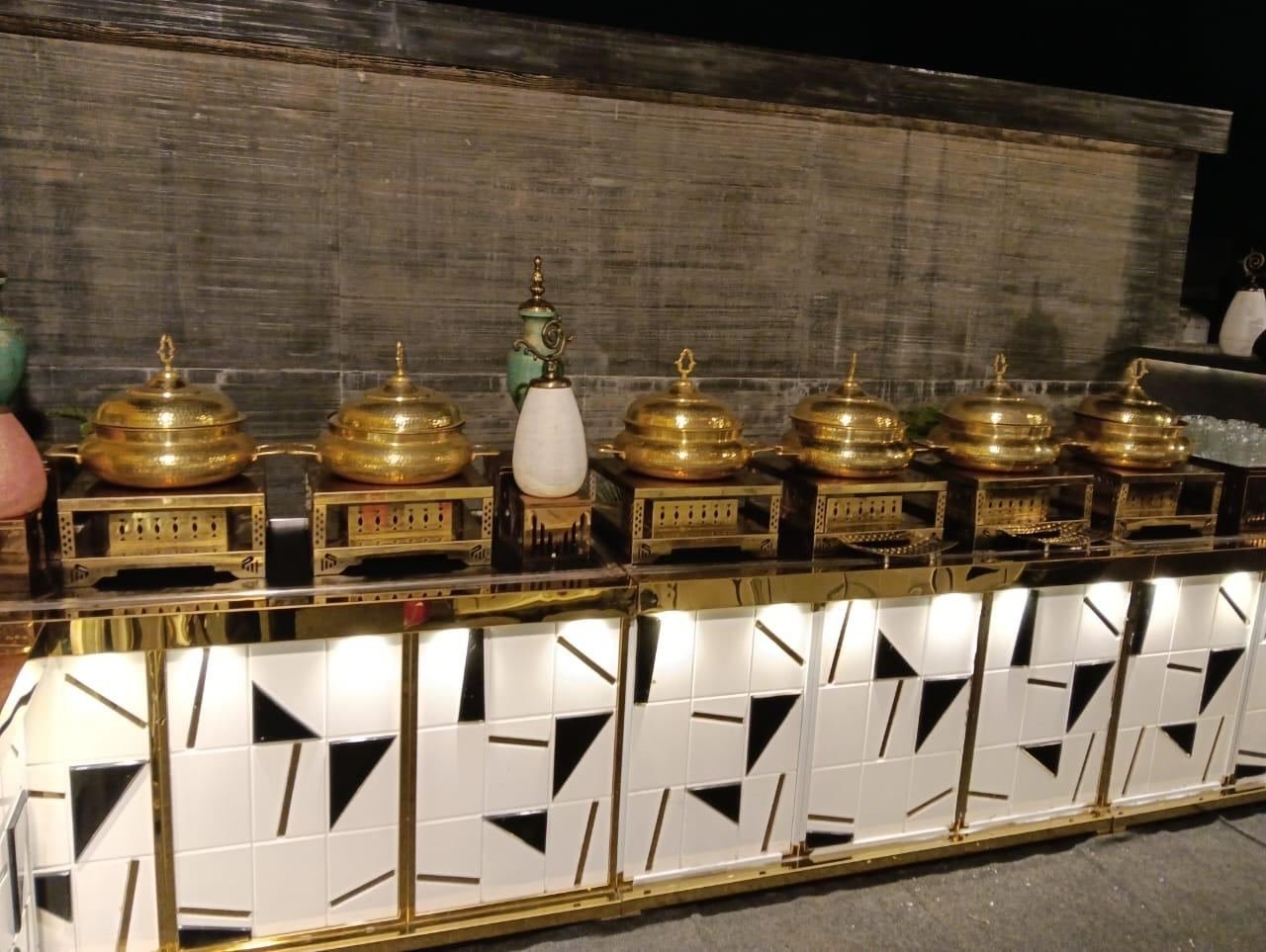 Brass handis on a lit black-and-gold buffet counter at an evening function