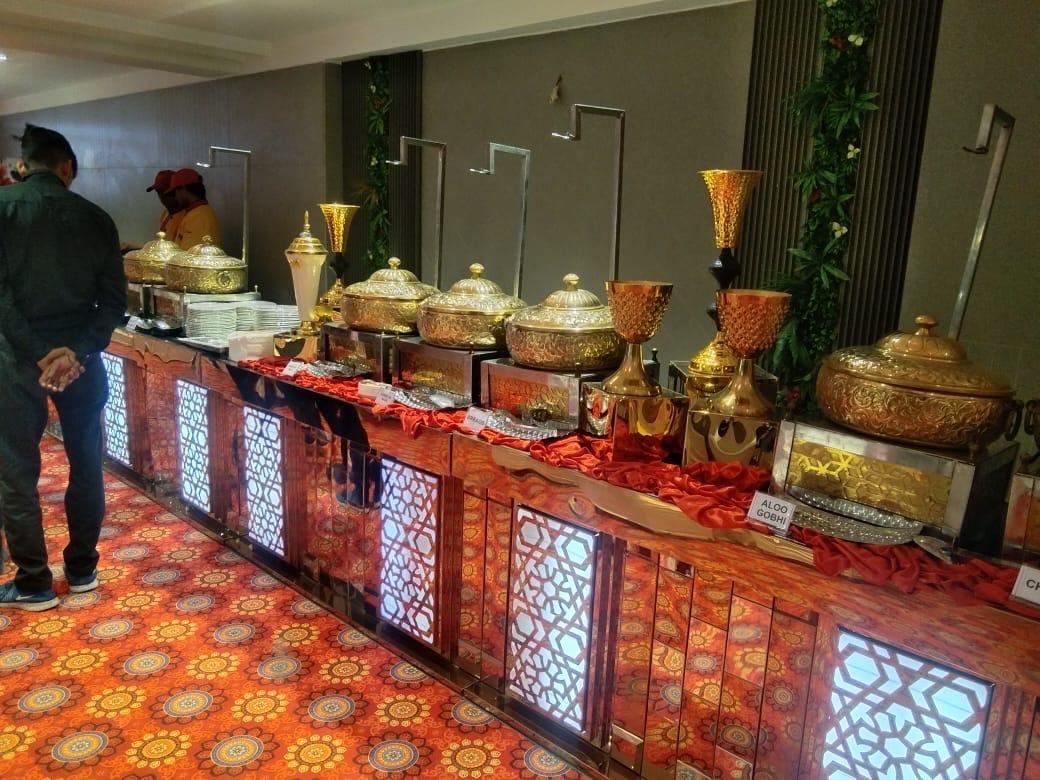 Long illuminated buffet counter with brass serving vessels and dish labels