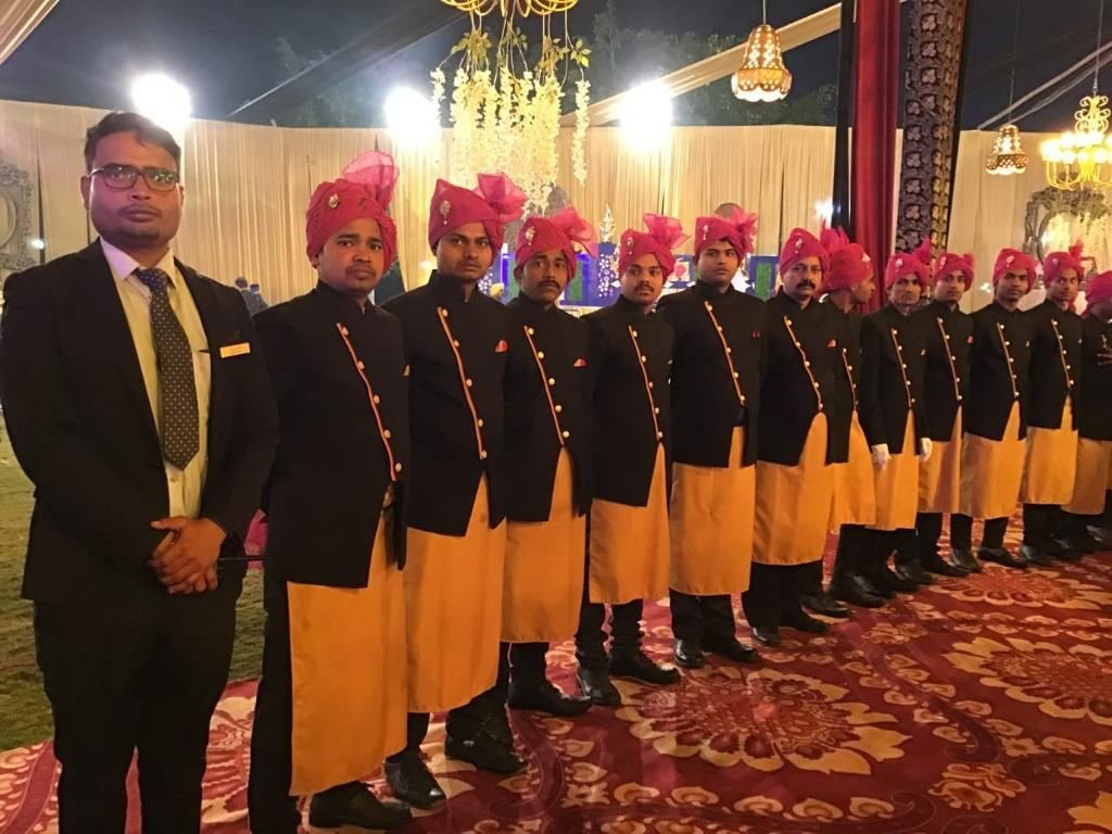 Service team lined up in black and gold uniforms with red safas before a function