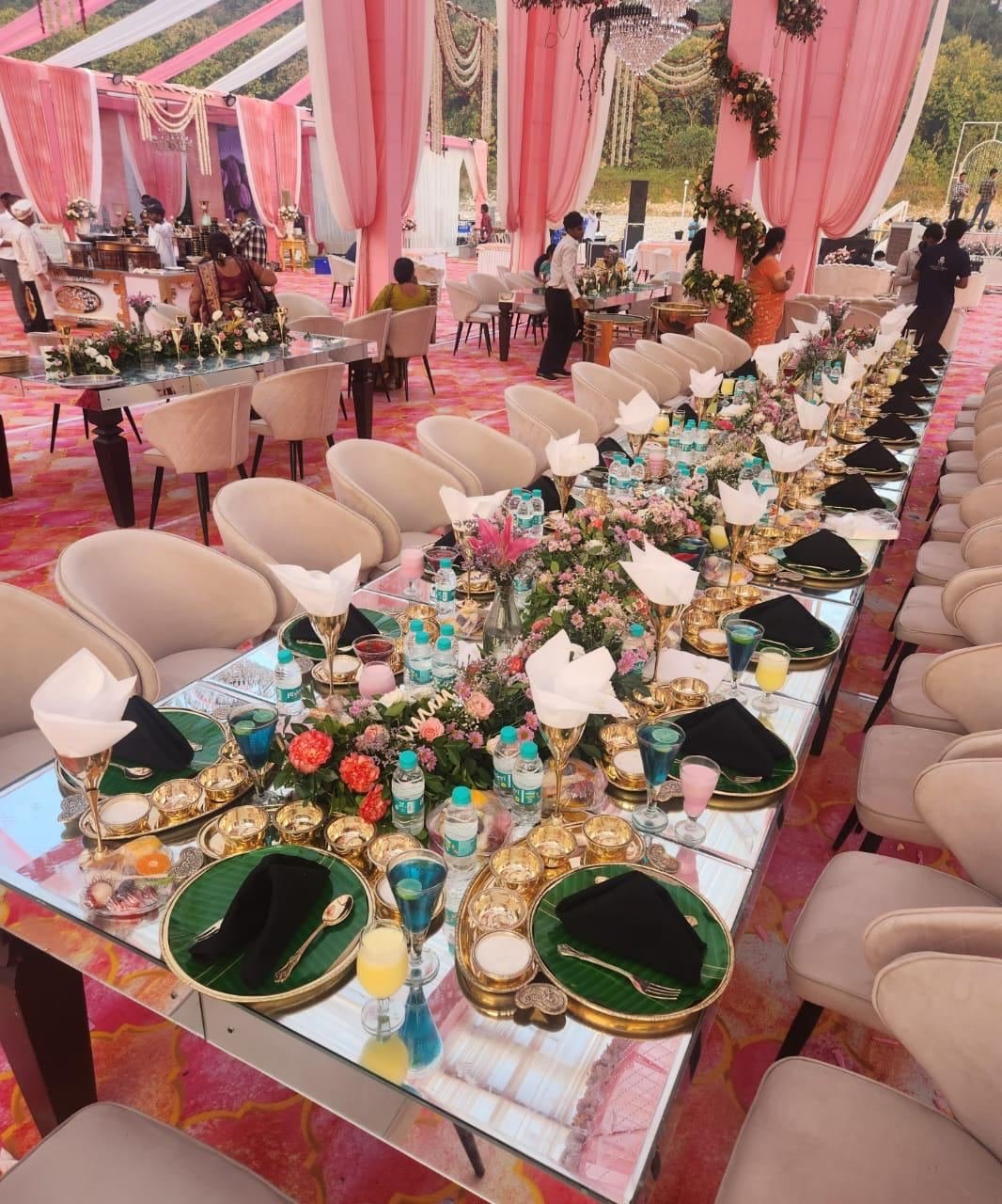 Long mirrored wedding table laid with gold thalis, banana leaves, napkins and flowers